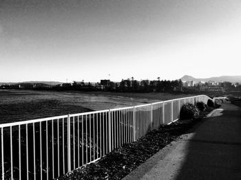 Footpath by river in city against clear sky