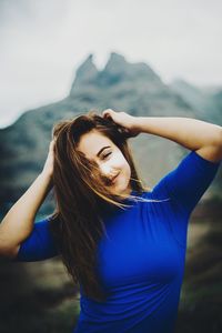 Portrait of young woman with arms raised against sky