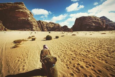Rear view of man walking with camel in wadi rum