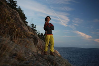 Full length portrait of woman standing on rock by sea