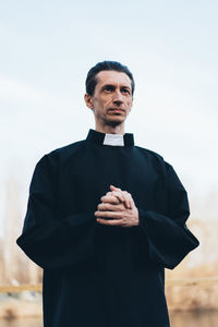 Priest looking away while standing against sky
