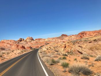 Road amidst desert against clear blue sky