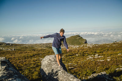 Woman standing on rock looking at mountain against sky