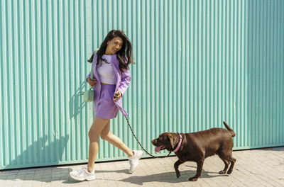 Full length of woman with dog standing against wall