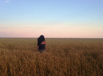 Rear view of woman amidst crops in field against sky