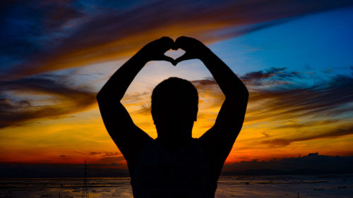 Silhouette man with heart shape standing by sea against sky during sunset