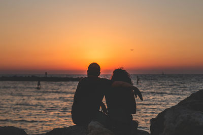 Silhouette friends on sea against sky during sunset