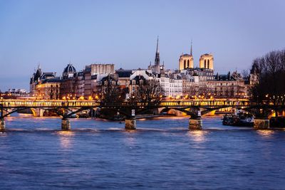 Illuminated buildings by river against sky in city