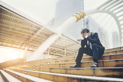 Full length of stressed businessman sitting on staircase in city