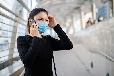 Businesswoman wearing mask talking on phone while standing on footbridge