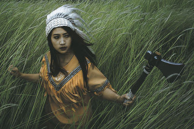 Woman in costume holding axe amidst grass