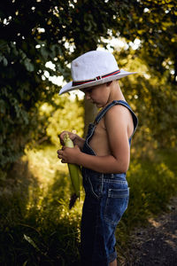 Side view of boy wearing hat standing by tree