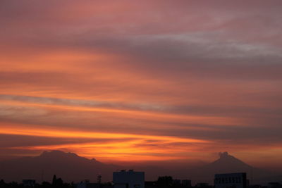 Silhouette buildings against dramatic sky during sunset