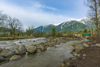 Scenic view of stream by snowcapped mountains against sky