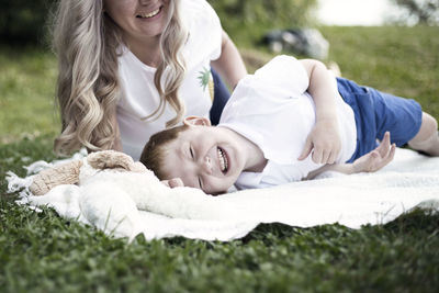 Mother and boy lying on grass against sky