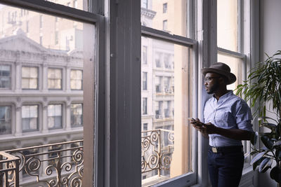 Businessman using mobile phone while standing by window in creative office