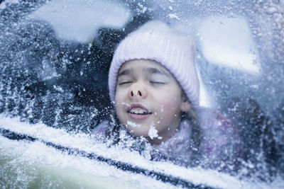 Playful girl touching nose on glass with snow