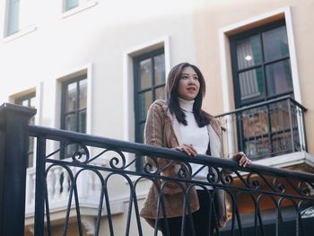 Young woman looking away while standing against railing