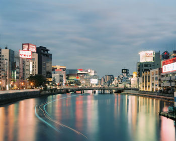 Illuminated buildings and river against sky in dynamic city