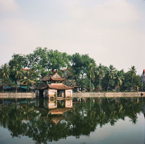 Reflection of house and trees by lake against sky