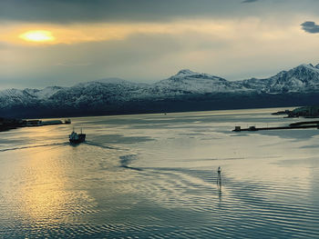Scenic view of lake by snowcapped mountains against sky during sunset