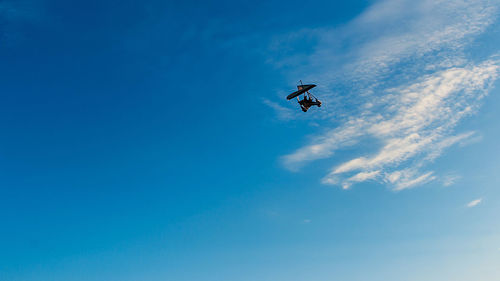 Low angle view of person hang-gliding against blue sky