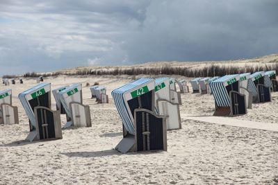 Hooded beach chairs on sand against sky