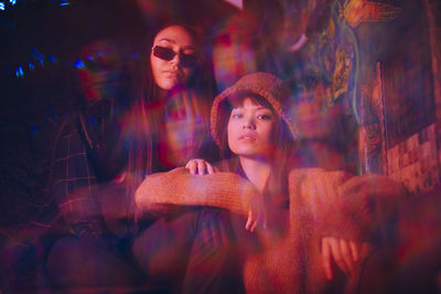 Multiple exposure of young female friends sitting together at illuminated restaurant