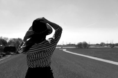 Rear view of woman wearing hat standing on road against sky during sunny day