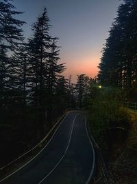 Road amidst trees in forest against sky at sunset