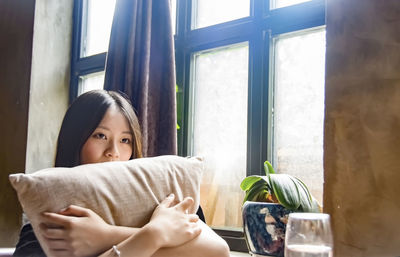 Woman holding pillow while sitting at home