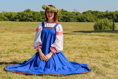 Portrait of young woman wearing flower tiara kneeling on field