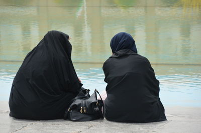 Women in burka sitting against lake