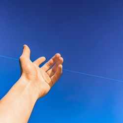 Low angle view of hands against clear blue sky