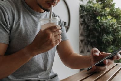 Midsection of man drinking lemonade while using mobile phone