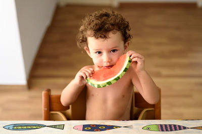 Portrait of shirtless girl eating watermelon at home