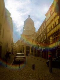 Cars on street by buildings against sky in city