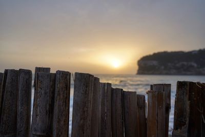 Panoramic shot of wooden post on sea against sky during sunset