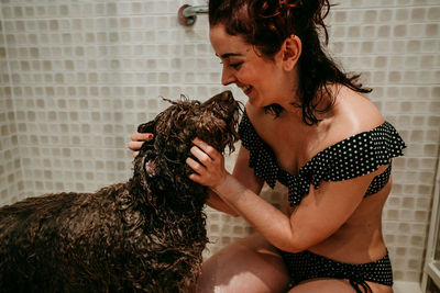 Smiling woman cleaning dog in bathroom