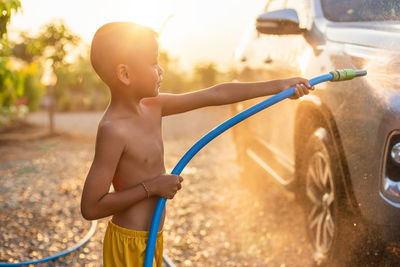 Shirtless boy cleaning car on sunny day
