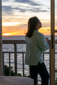 Side view of woman standing by sea against sky during sunset