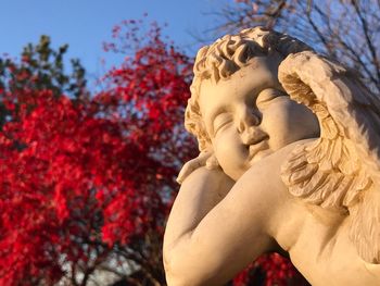 Low angle view of angel sculpture against red tree at park
