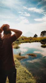 Rear view of woman standing by lake against sky