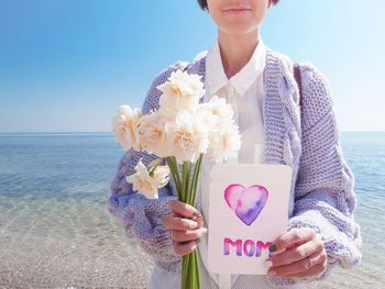 Young woman holding flower bouquet against sea
