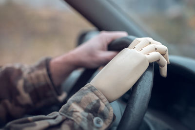 Cropped hand of soldier holding steering wheel with prosthetic hand