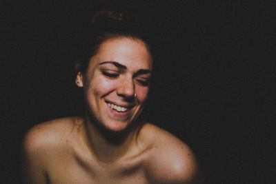 Smiling topless young woman against black background