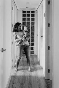 Smiling mother holding daughter at entrance of home