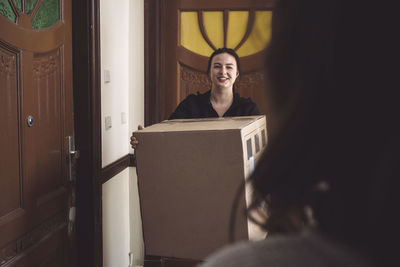 Smiling delivery woman delivering package to customer at doorstep