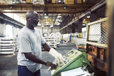 Side view of blue collar worker using control machine while working in steel industry