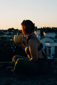 Woman drinking with a melon on the rooftop during sunset
